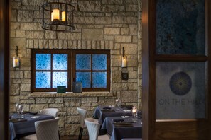 A restaurant with stone walls, a large window with frosted glass, and candle-lit tables.