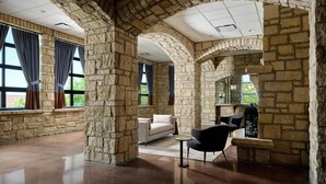 Amplia habitación con arcos de piedra, ventanas grandes con cortinas, un sofá, una silla y una mesita.