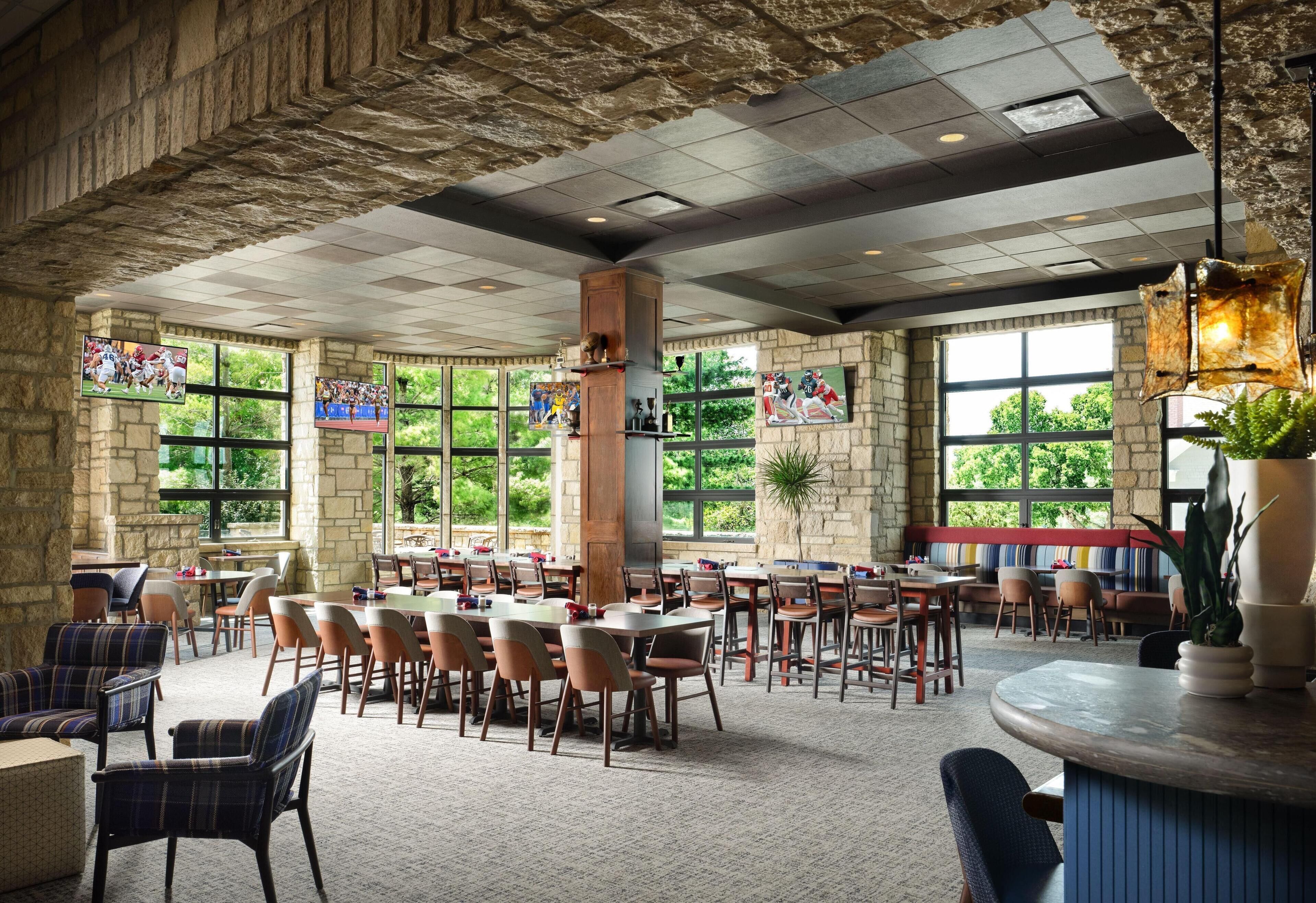 A spacious indoor dining area with stone walls, large windows, and multiple tables and chairs.