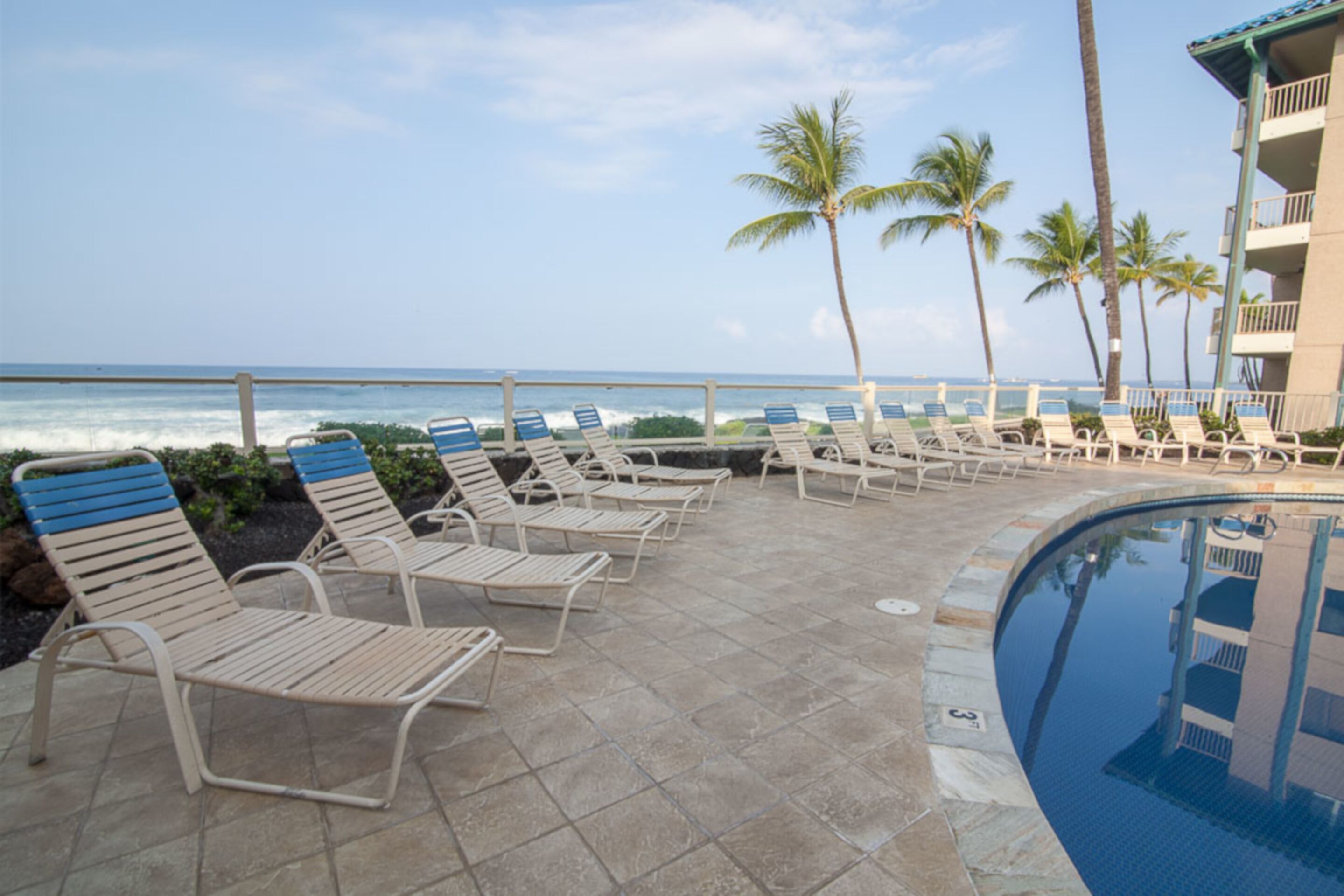 A poolside area with lounge chairs and a view of the ocean.