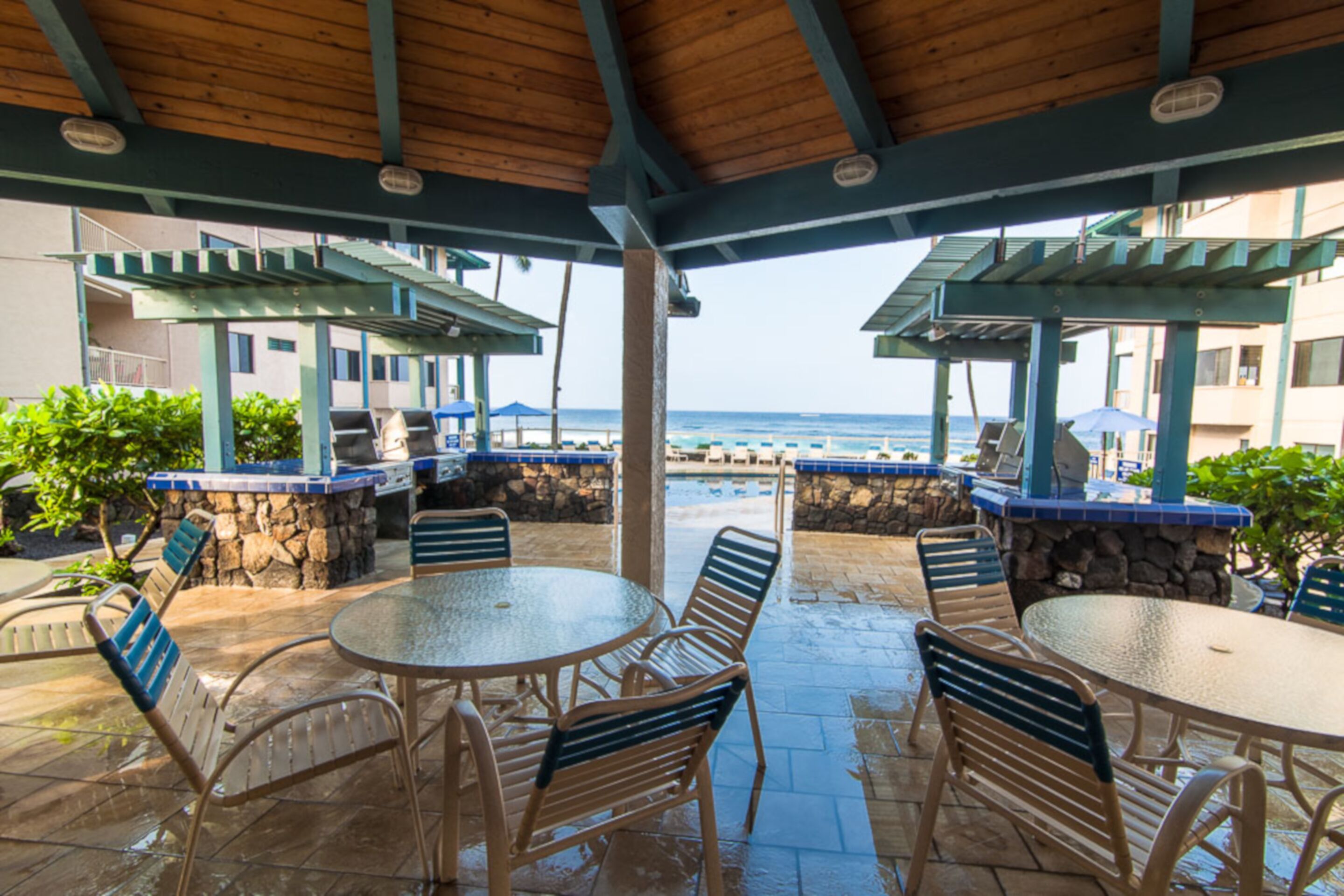 An outdoor patio area with round tables and chairs, a stone wall, and a view of the ocean.