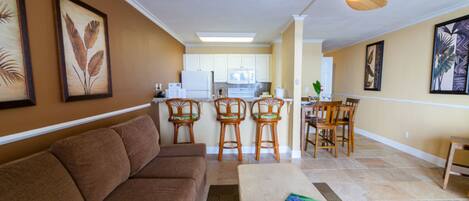 A living room with a brown sofa, a coffee table, and a dining area with wooden chairs and a table.