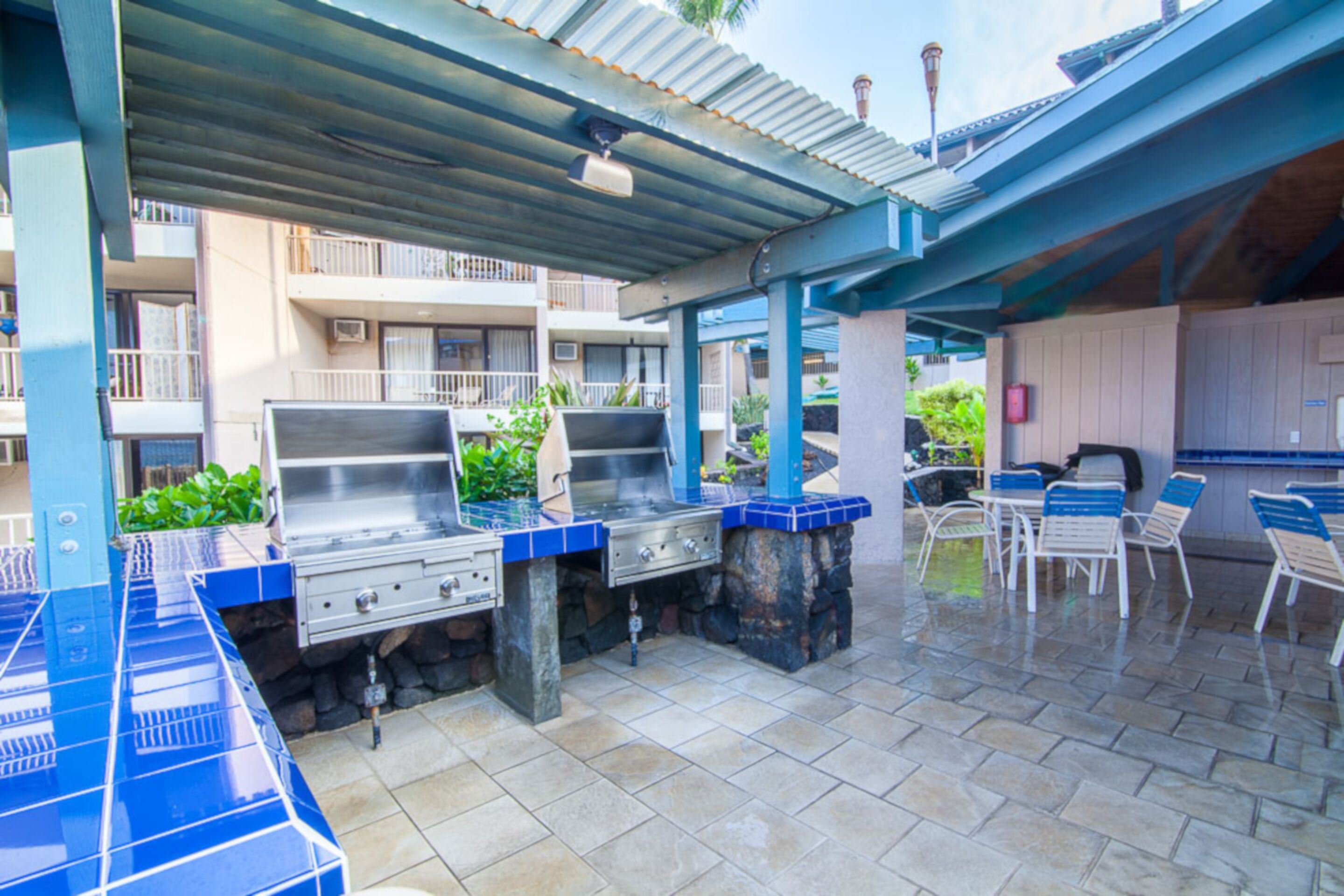 An outdoor patio with a barbecue grill, seating area, and a covered section with a view of a building in the background.