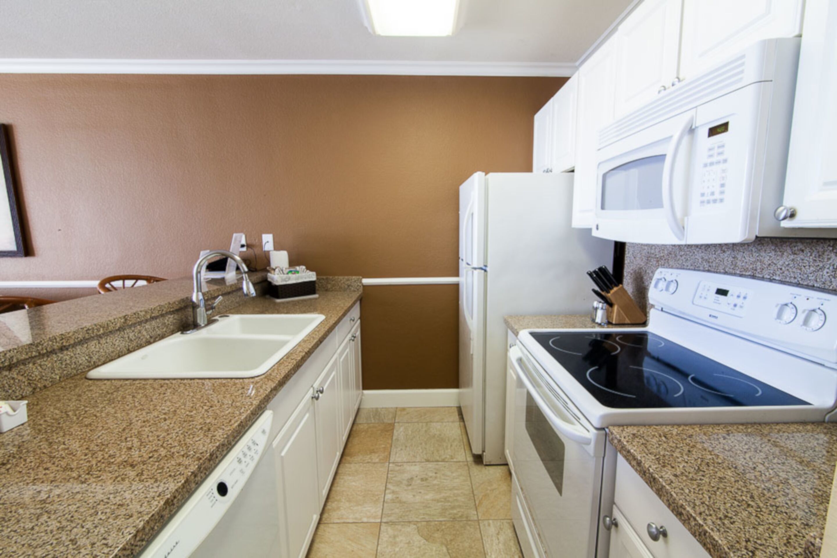 A compact kitchen with a sink, stove, microwave, and granite countertops.
