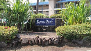 Une enseigne pour Kona Reef, avec un palmier et, en arrière-plan, un bâtiment aux toits bleus.