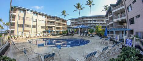 A hotel with a pool area, lounge chairs, and palm trees.