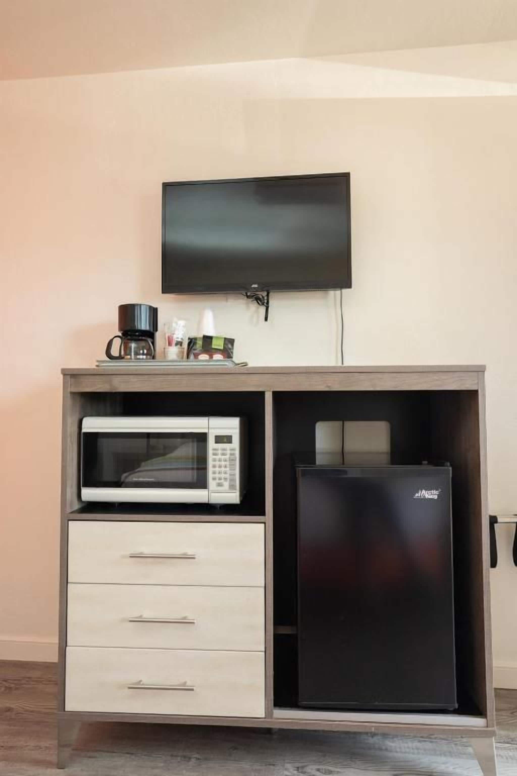 A kitchenette with a microwave, refrigerator, and a flat-screen TV mounted on the wall.