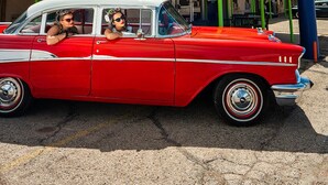 Une voiture rouge d’époque est garée devant un bâtiment sur lequel on peut lire l’inscription « The Atomic Blues Motor Inn ».