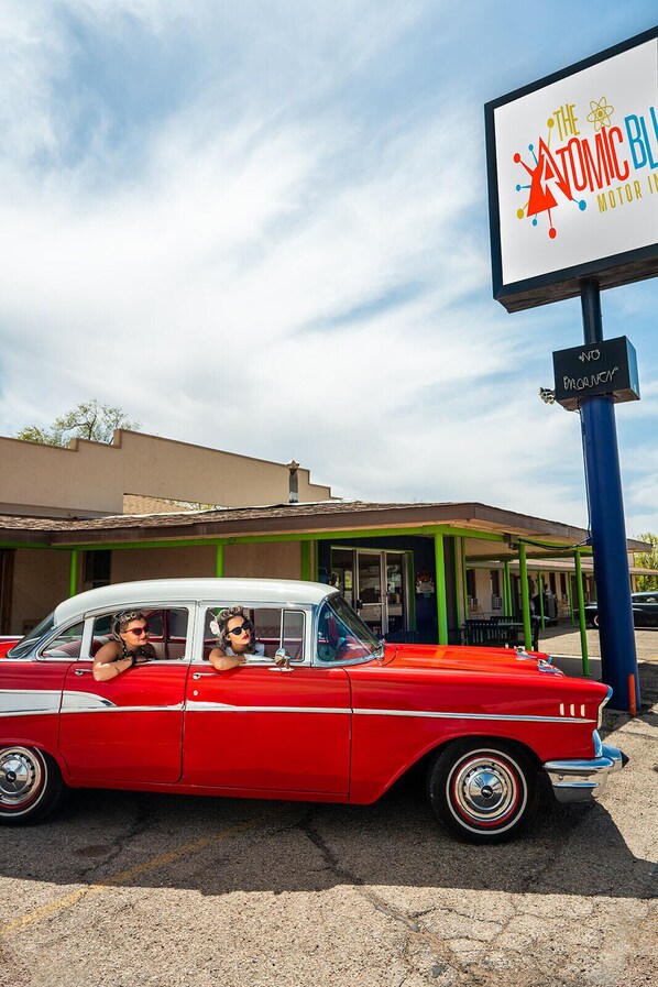Une voiture rouge d’époque est garée devant un bâtiment sur lequel on peut lire l’inscription « The Atomic Blues Motor Inn ».