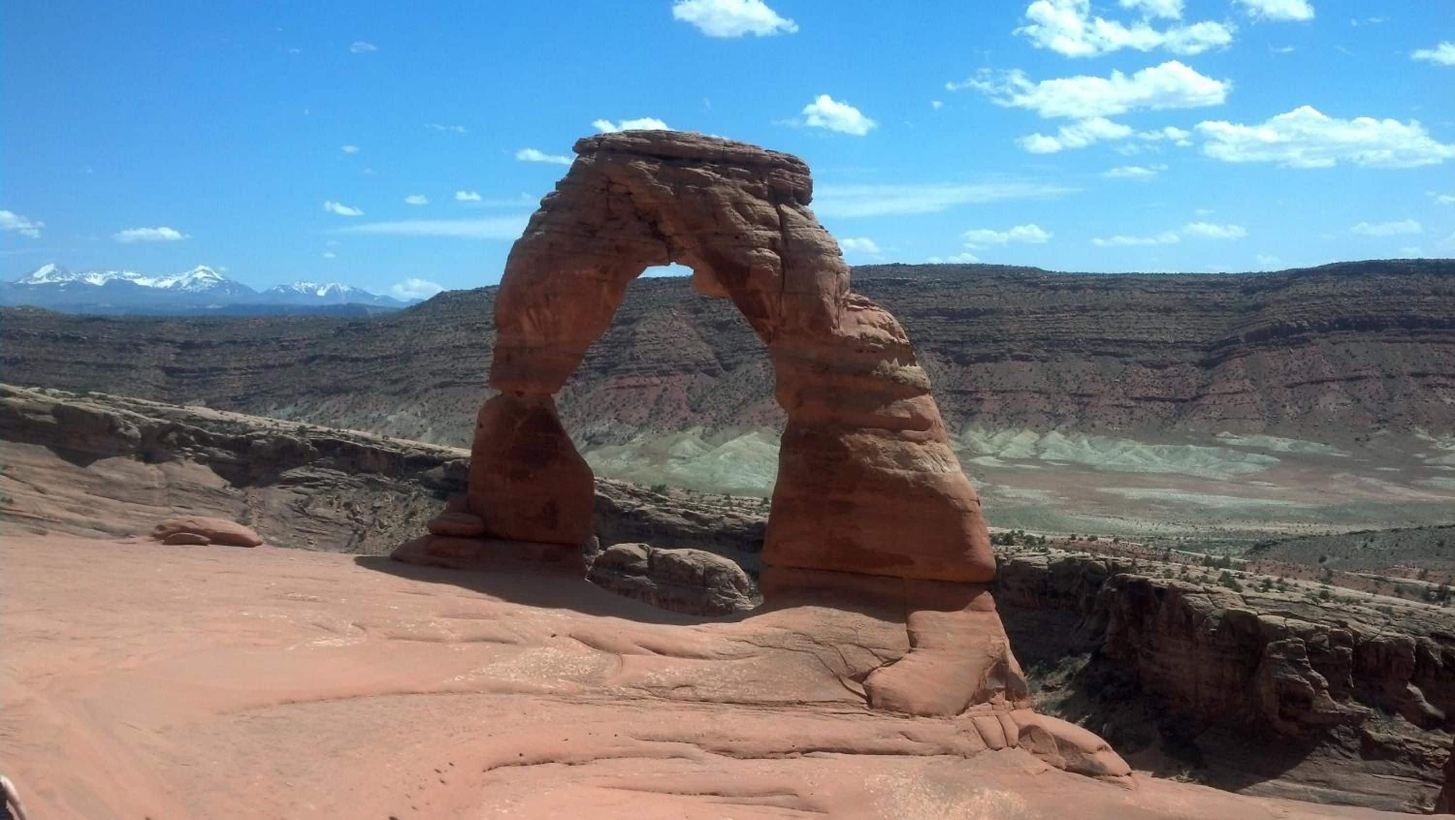 Une arche naturelle formée par la roche, avec un ciel dégagé et des montagnes lointaines.