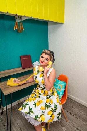 A person sitting on a chair in a room with a teal wall, a wooden desk, and a yellow telephone. - The Atomic Blue Motor-Inn (Monticello)