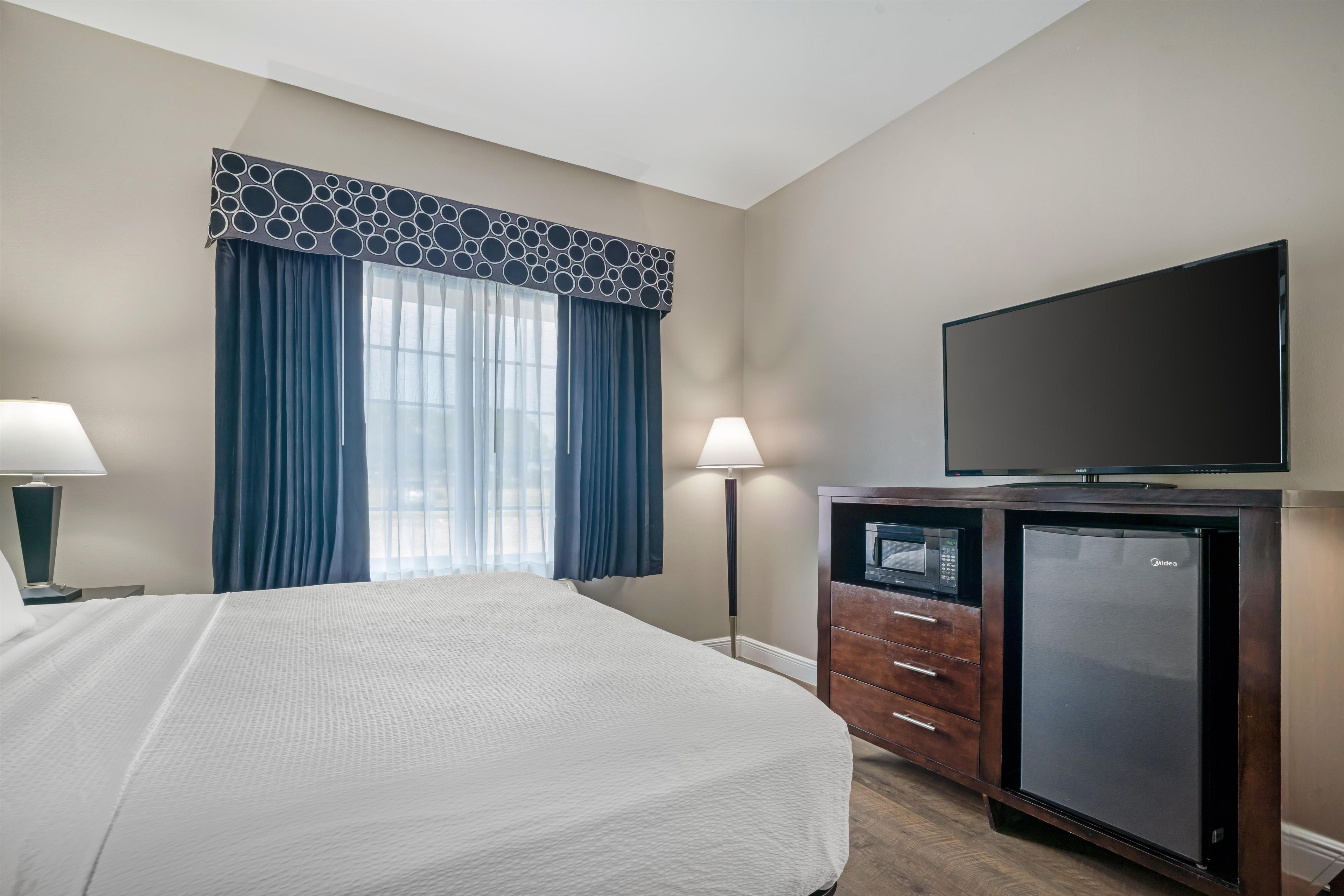 A hotel room with a bed, a flat-screen TV, a minibar, and a window with curtains.