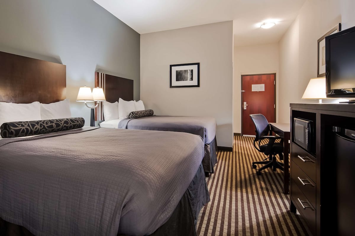 A hotel room with two beds, a desk with a computer, a TV, and a microwave.