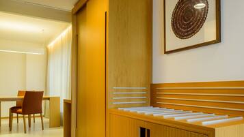 A modern hotel room with a wooden cabinet, a dining area with a table and chairs, and a framed artwork on the wall.