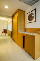A modern hotel room with a wooden cabinet, a dining area with a table and chairs, and a framed artwork on the wall.