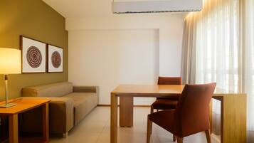 Una habitación de hotel moderna con una mesa de comedor de madera, un sofá, una lámpara y dos cuadros en la pared.