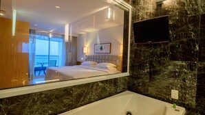 A modern hotel room with a large bathtub, a television mounted on the wall, and a balcony visible through the window. - Hotel Luzeiros São Luis (São Luís)