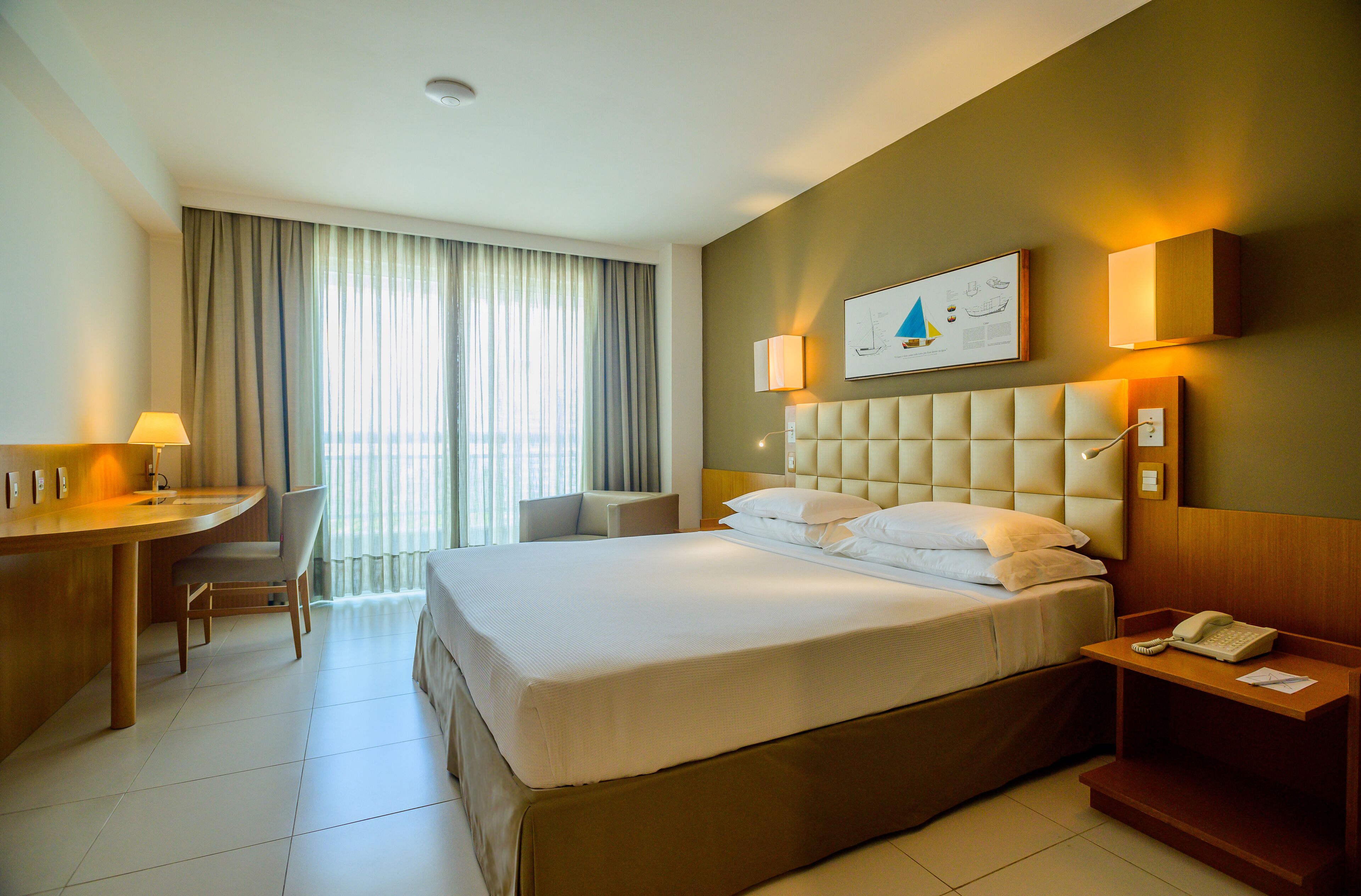 A hotel room with a bed, a desk, a chair, a nightstand, and a window with curtains.