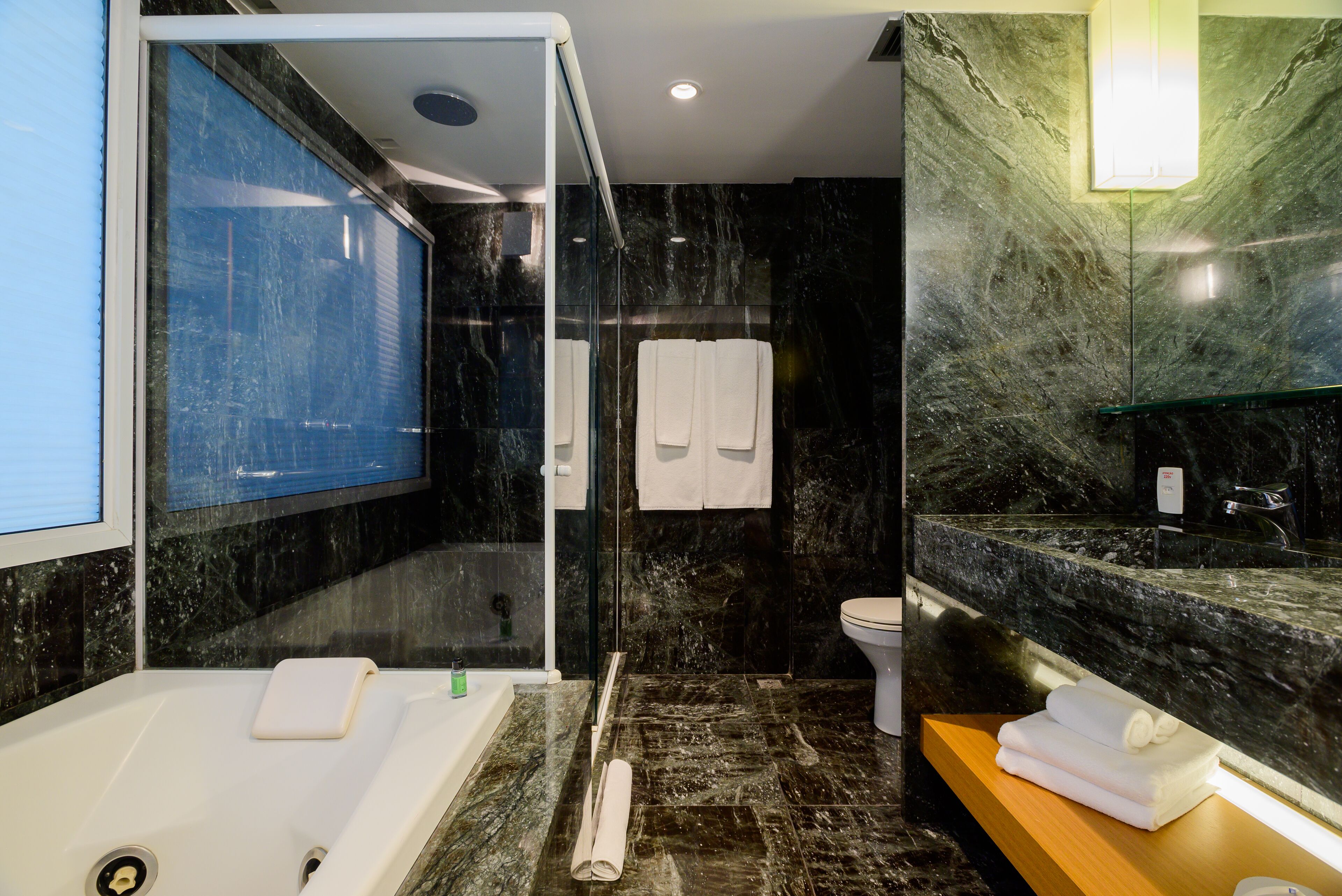 A modern bathroom with a glass-enclosed shower, a white bathtub, and a marble countertop.
