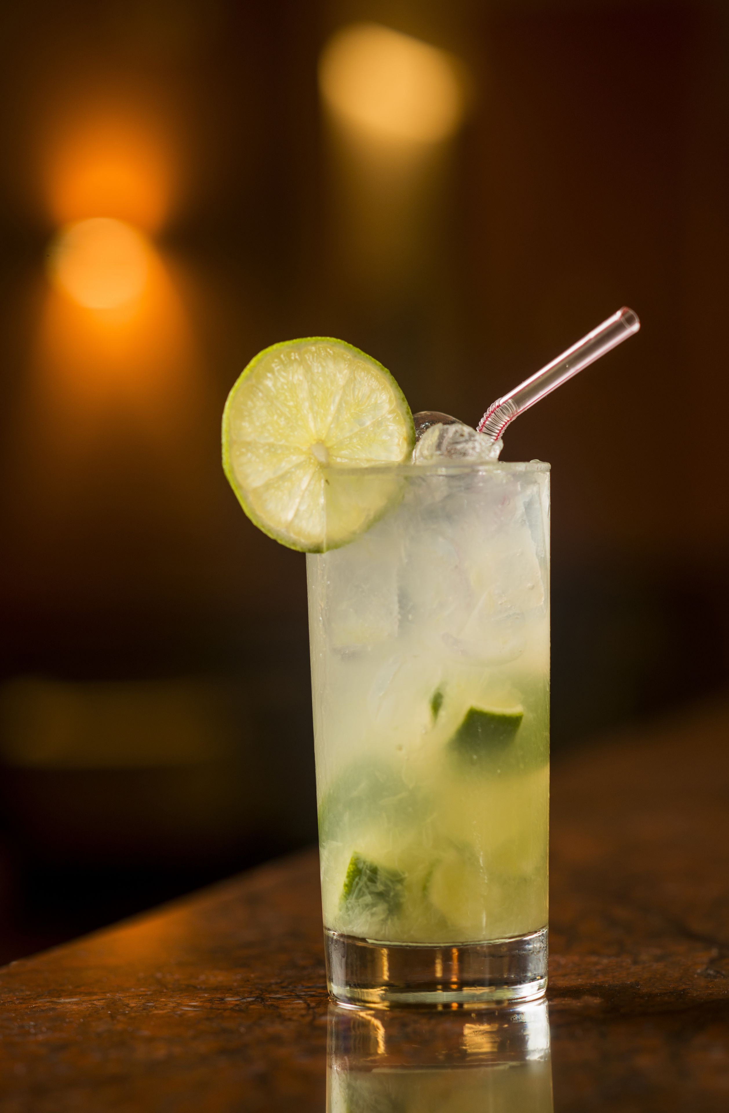 A tall glass with a lime slice and a straw, filled with ice and possibly mint leaves, on a reflective surface.
