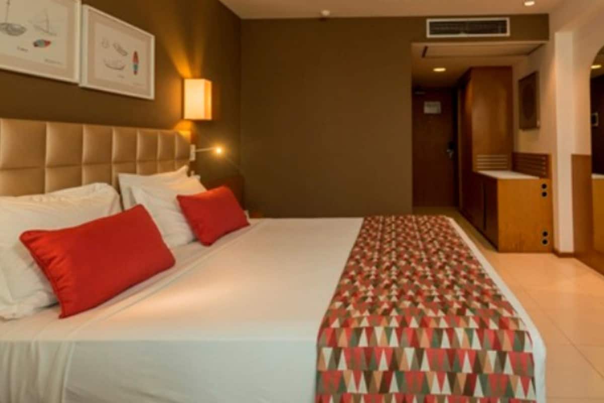 Habitación de hotel con una cama grande, un televisor y un baño visible a través de un arco.