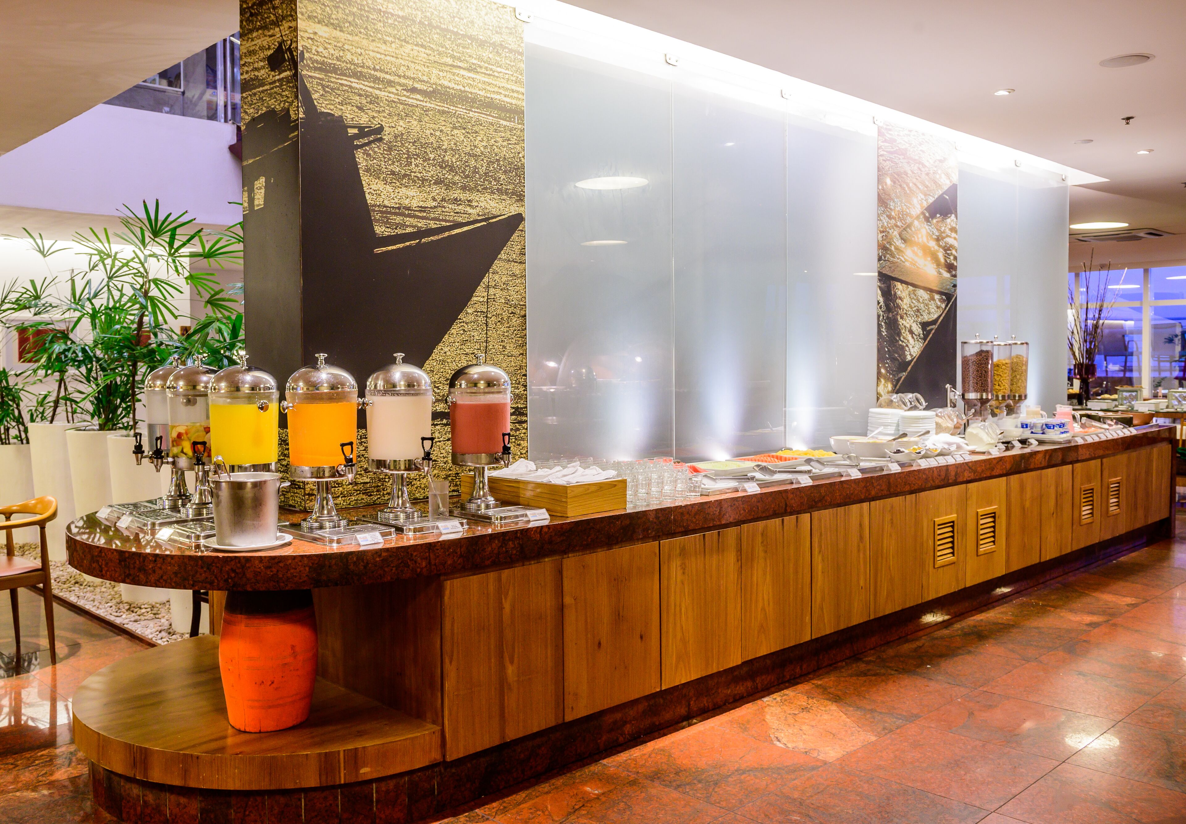 A hotel reception area with a long counter, various food and drink dispensers, and a large decorative wall.