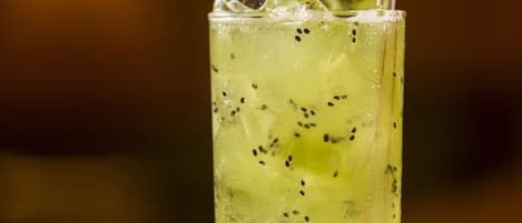 Un grand verre avec une paille, contenant une boisson jaune et de petites graines noires, posé sur une surface réfléchissante.