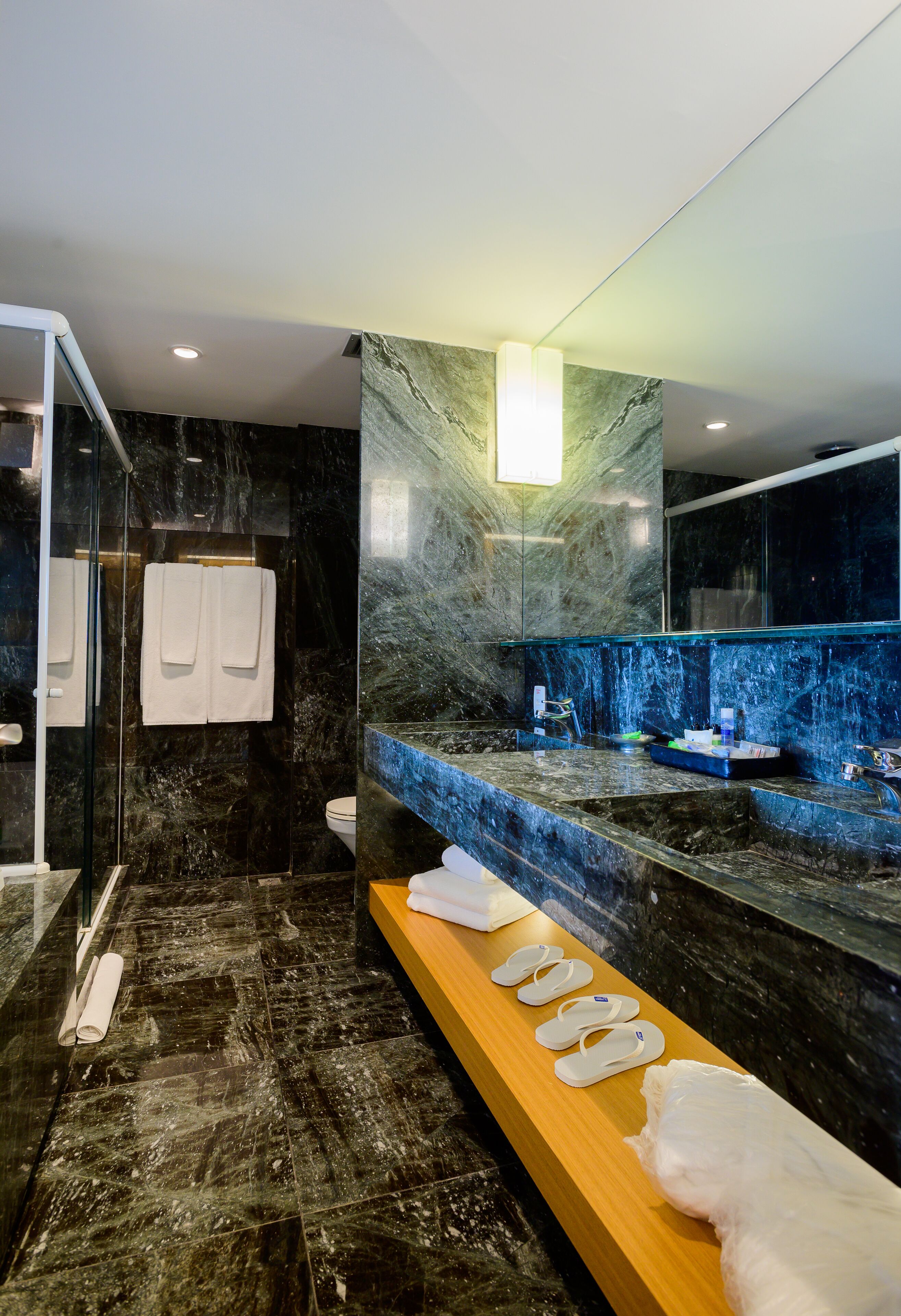 A modern bathroom with a marble floor, a wooden vanity, a glass shower enclosure, and a large mirror.