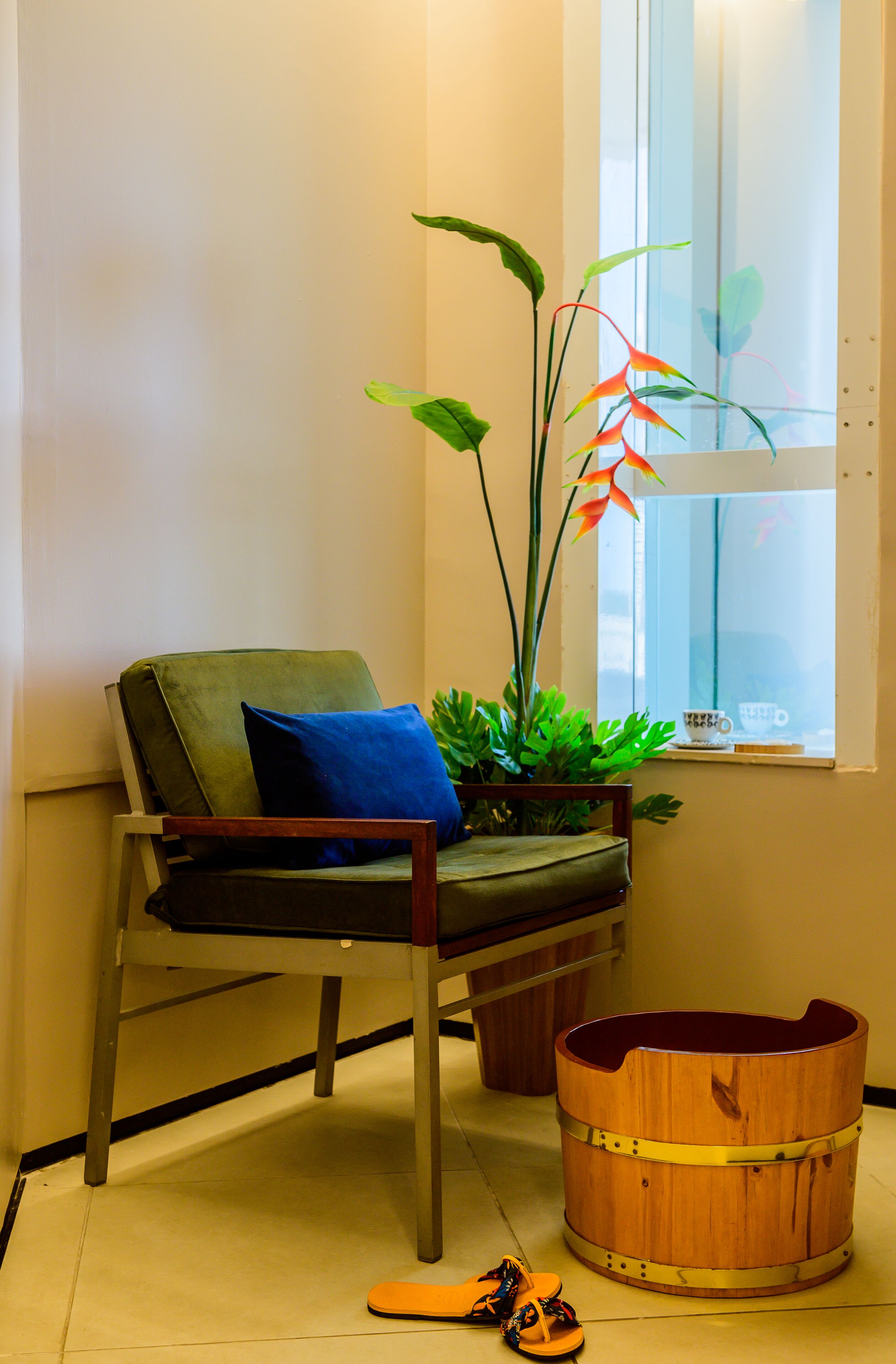 Una silla con cojín, una planta en maceta y un cubo de madera en una habitación con ventana.