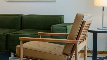 A room with a green sofa, a wooden chair, a lamp, and a colorful abstract painting on the wall.