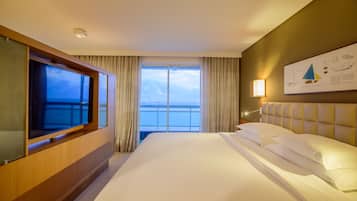 A hotel room with a large bed, a TV, a view of the sea, and a framed picture on the wall.