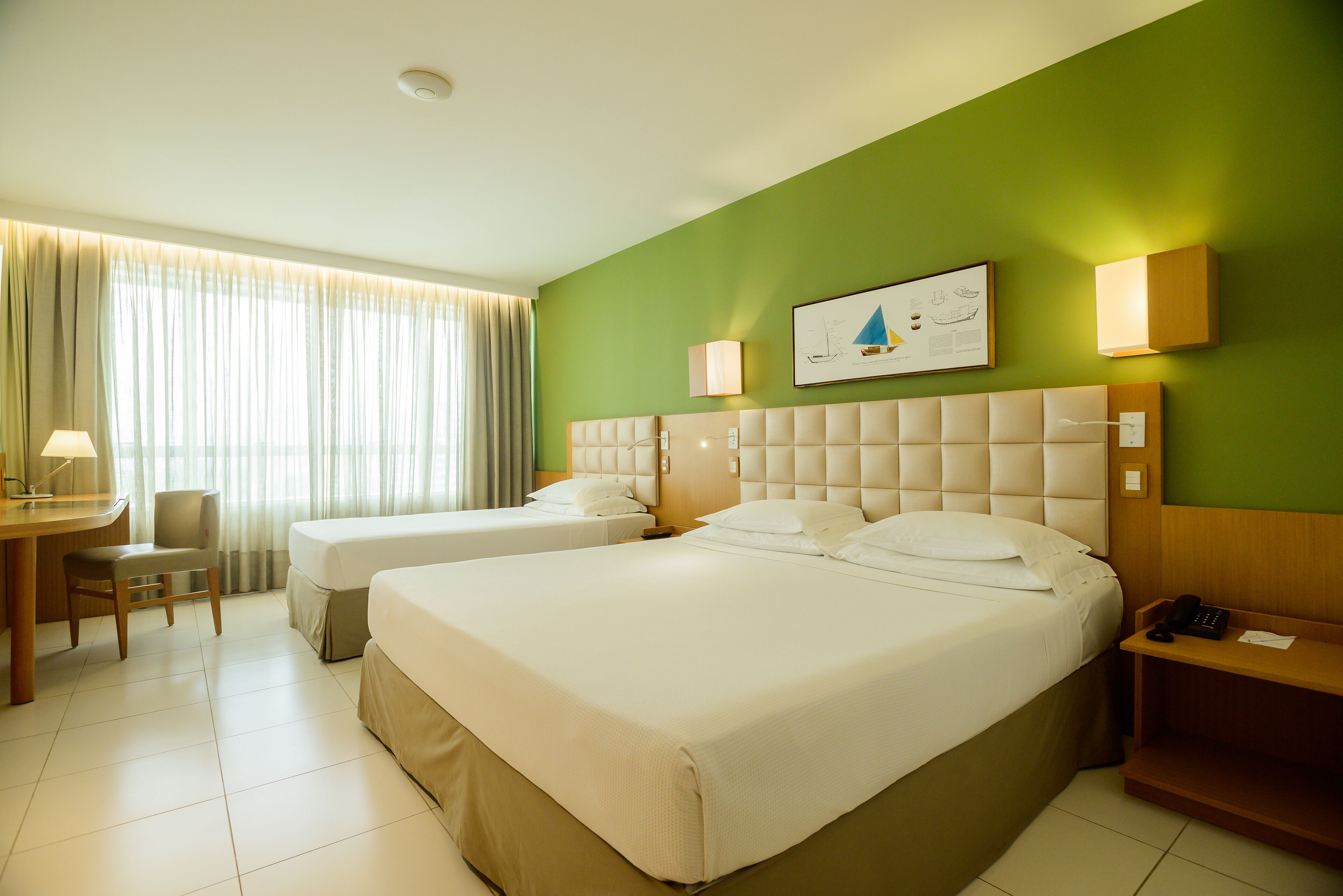 A hotel room with two beds, a desk, a chair, and a green wall.