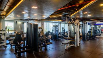 A gym with various exercise machines, large windows, and a high ceiling with exposed ductwork.
