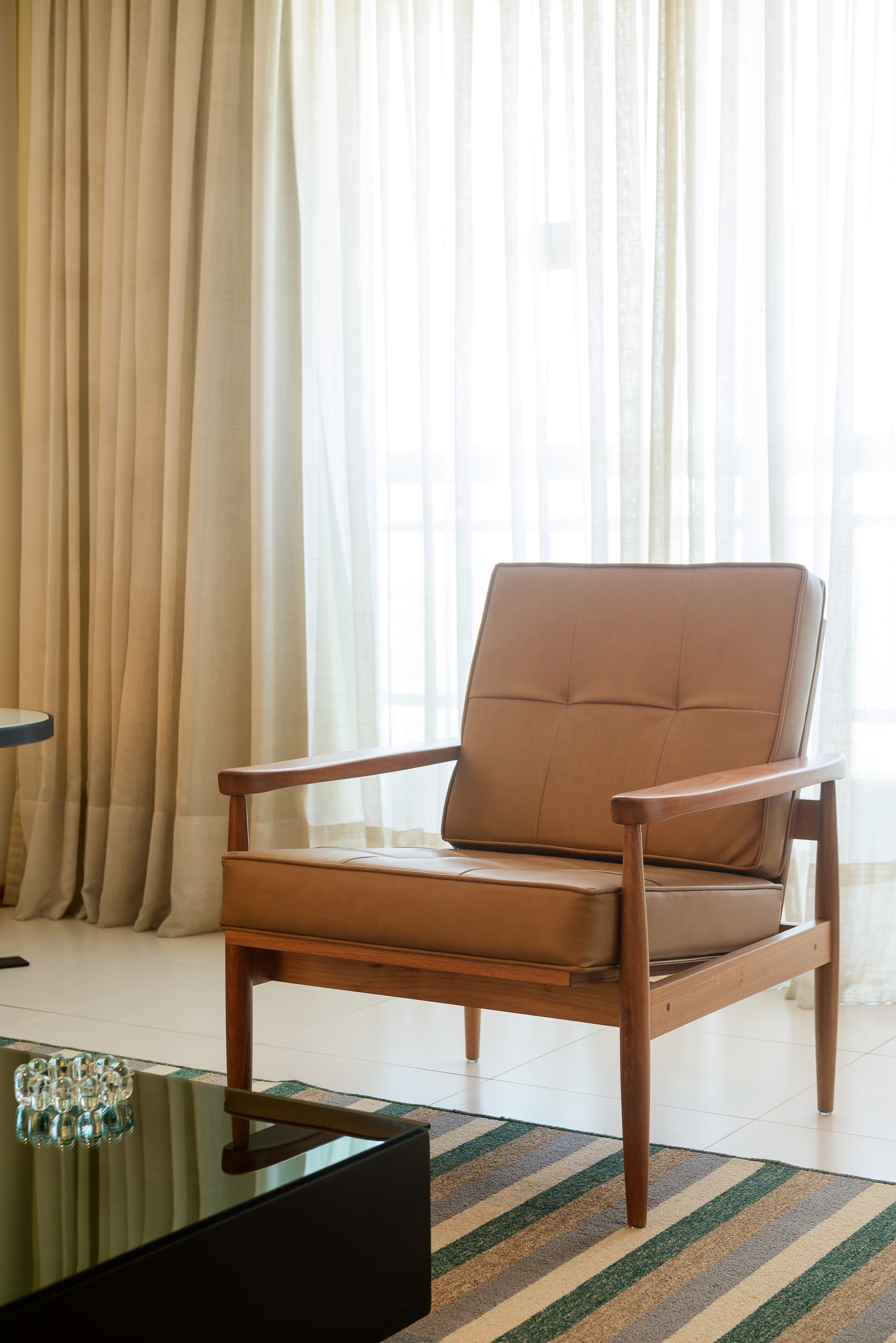 A modern living room with a brown leather armchair, a glass coffee table, and a striped rug.