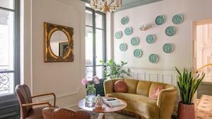 A room with a sofa, chairs, a round table, a mirror, a chandelier, and decorative plates on the wall. - Hotel de la Porte Dorée (Paris)