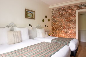 A hotel room with two beds, a brick wall, a framed picture, and a flower vase. - Hotel de la Porte Dorée (Paris)
