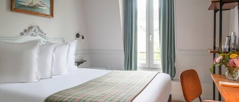 Una habitación de hotel con cama, escritorio, silla, ventana con cortinas y un cuadro en la pared.