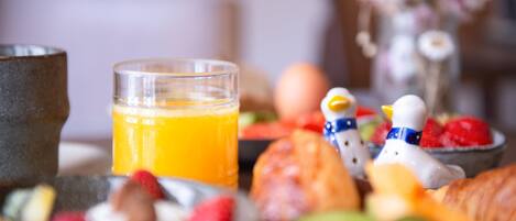 A breakfast setting with a glass of orange juice, fruits, and pastries.