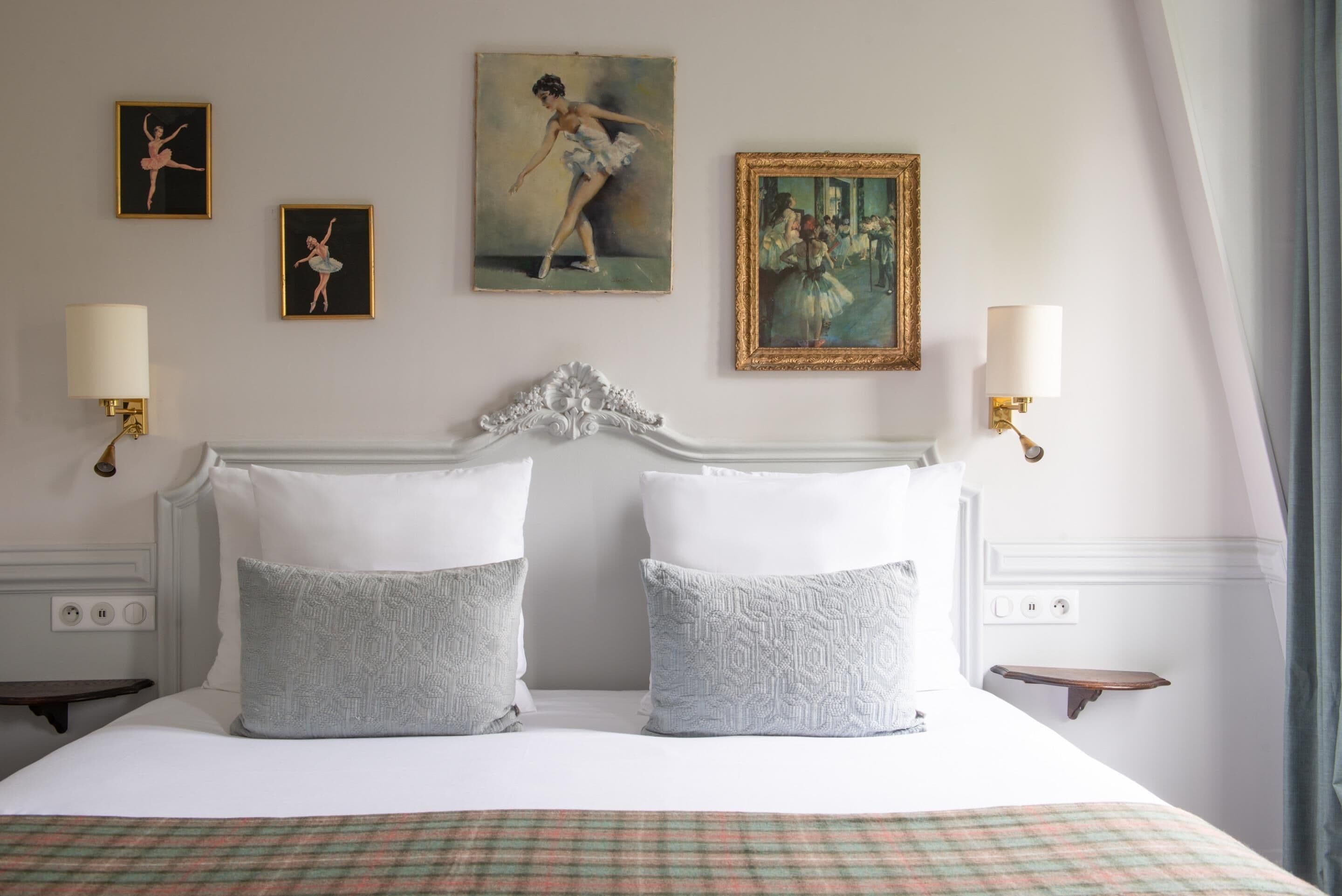 Une chambre d’hôtel avec un grand lit, deux lampes fixées au mur et trois tableaux encadrés accrochés au mur.
