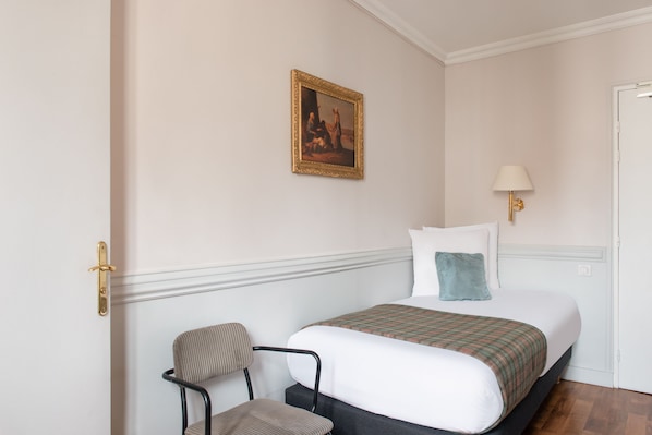 A hotel room with a bed, a chair, a painting on the wall, and a lamp. - Hotel de la Porte Dorée (Paris)