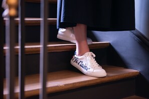 A person wearing white sneakers with "Tétane" on the side, descending a wooden staircase. - Hotel de la Porte Dorée (Paris)