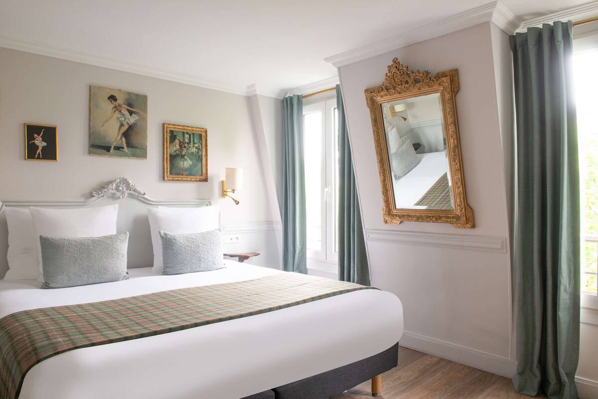A hotel room with a large bed, a mirror, and three paintings on the wall.