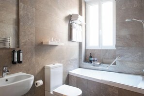 A modern bathroom with a sink, toilet, and bathtub. There is a window providing natural light, and toiletries are visible on the wall. - Hotel de la Porte Dorée (Paris)
