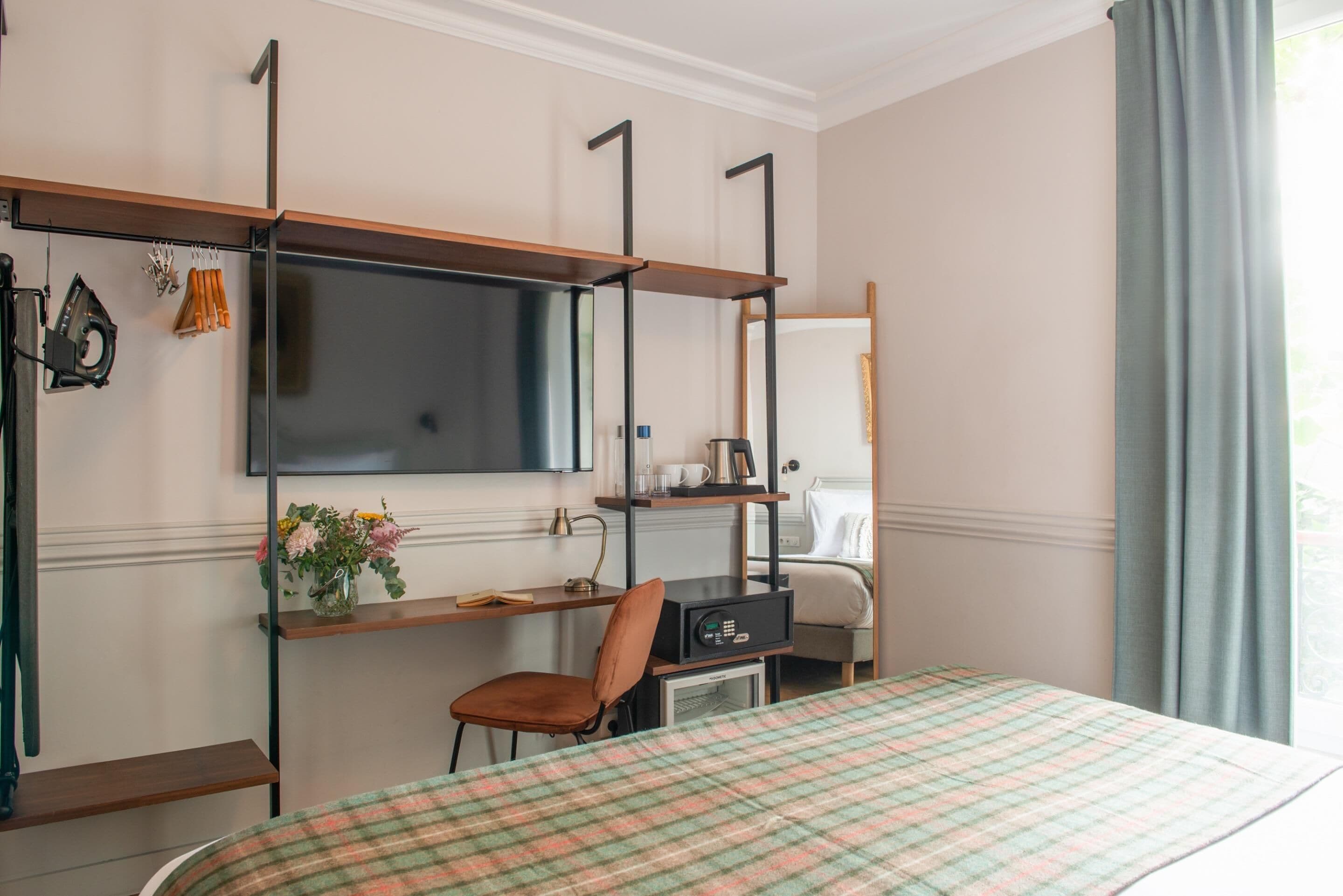 A hotel room with a bed, a desk with a chair, a television, and a window with curtains.