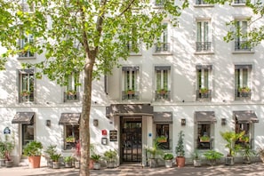 Un hotel de varios pisos con fachada clásica, grandes ventanales y plantas en macetas.