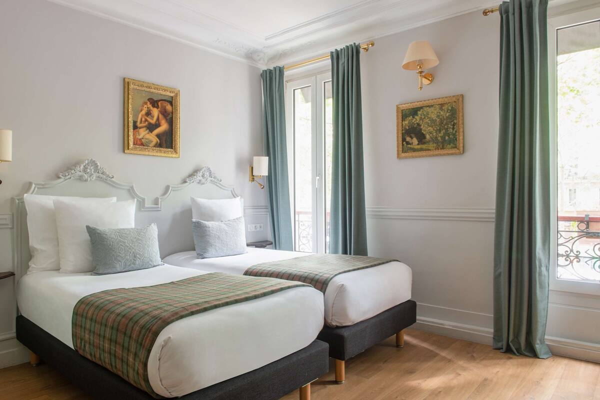 A hotel room with two beds, a window with curtains, and artwork on the walls.