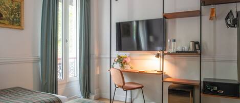 A hotel room with two beds, a desk with a chair, a flat-screen TV, a small kitchen area, and a window with curtains.