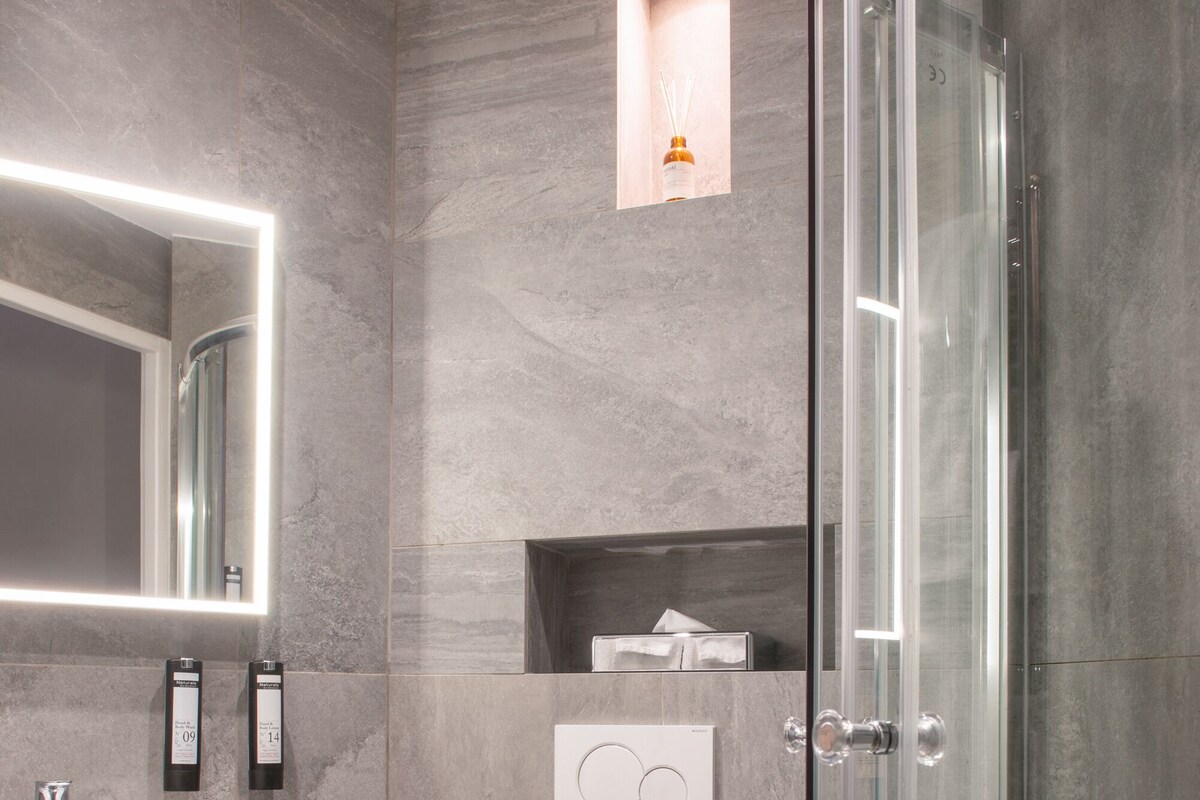 A modern bathroom with a glass-enclosed shower, a white toilet, and a marble-tiled sink area.