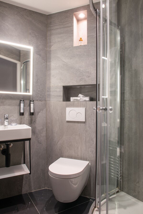 A modern bathroom with a glass-enclosed shower, a white toilet, and a marble-tiled sink area. - Hotel de la Porte Dorée (Paris)