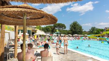 Zona de piscina con sillones de descanso y sombrillas.